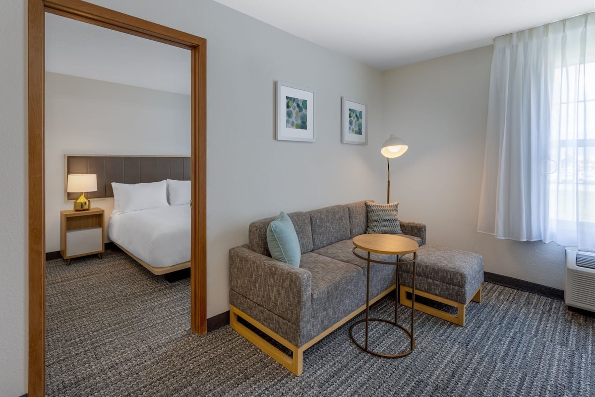 A hotel room with a bed, a gray sofa, a small round table, and two framed pictures on the wall.