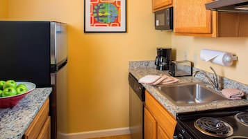 A kitchen with a refrigerator, microwave, stove, sink, and a bowl of green apples on the counter.