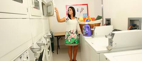 Uma lavanderia com várias máquinas de lavar, um cesto com detergente para roupa e uma mesa com um cesto de roupas dobradas.
