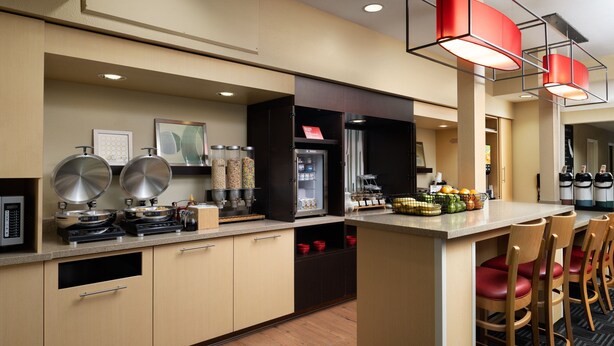 Una cocina moderna con electrodomésticos de acero inoxidable, una isla central con taburetes altos y un refrigerador con puerta de vidrio.