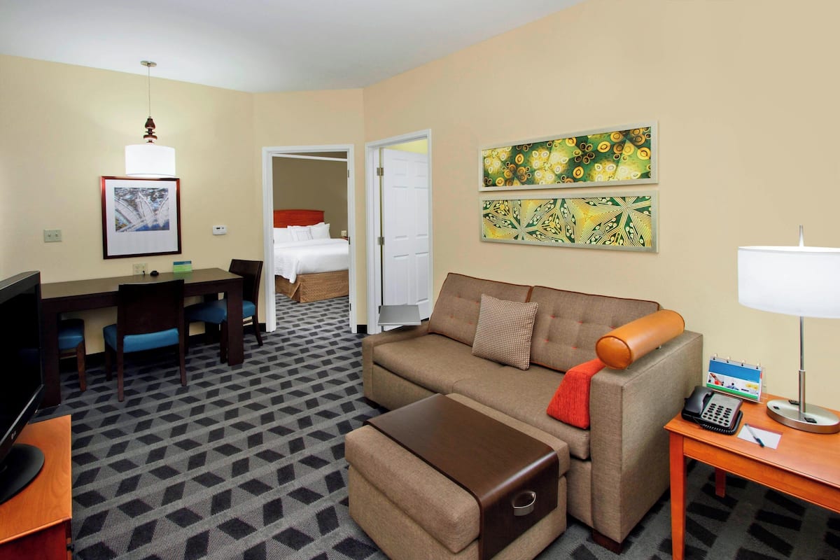Ein Hotelzimmer mit Sofa, Hocker, Schreibtisch, Fernseher und Kunstwerken an den Wänden.