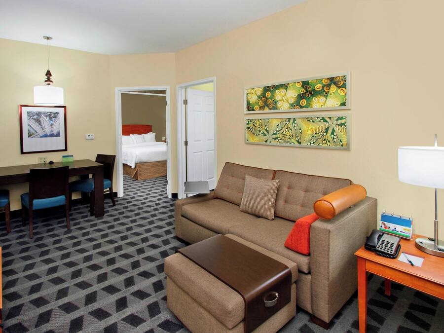 A hotel room with a sofa, ottoman, desk, television, and artwork on the walls.