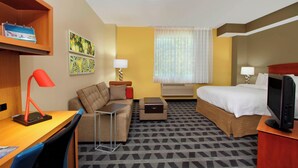 Habitación de hotel con cama, escritorio, silla y una mesita. Hay dos lámparas fijadas a la pared y una ventana con cortinas.
