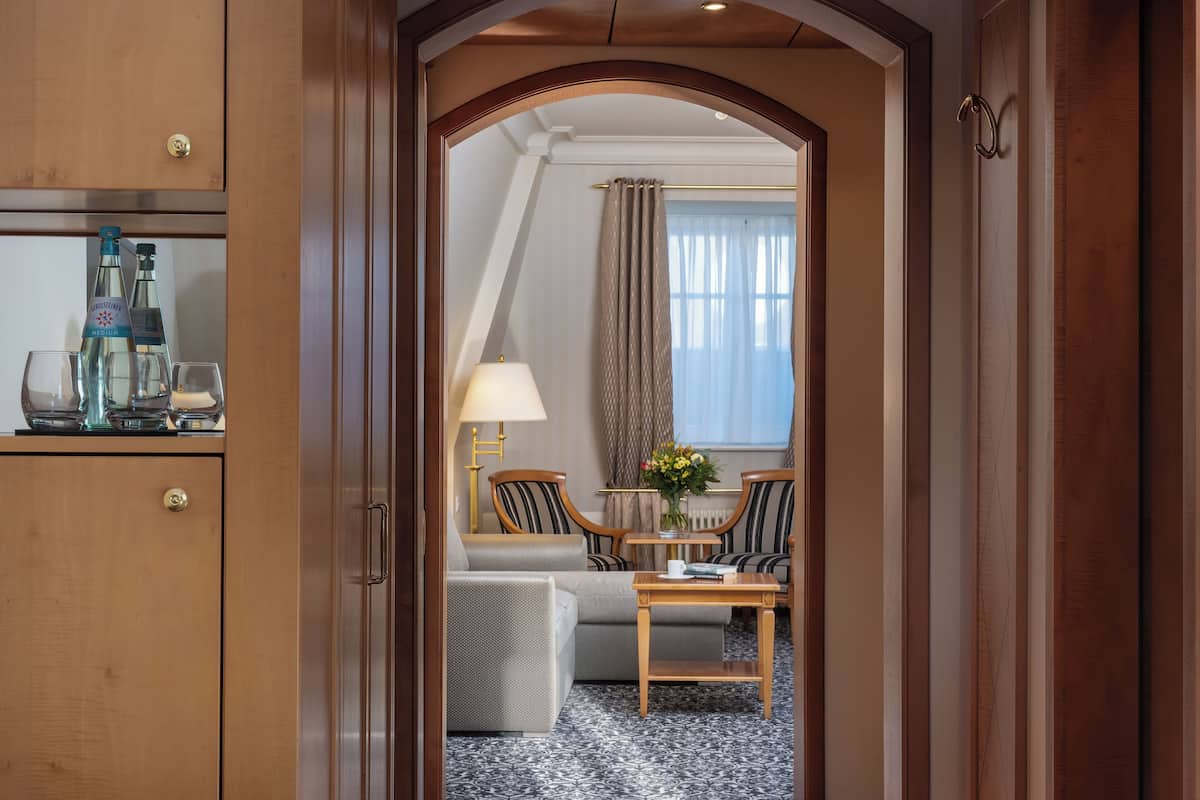 Una habitación de hotel con un armario de madera, un sofá, una mesa con lámpara y una ventana con cortinas.