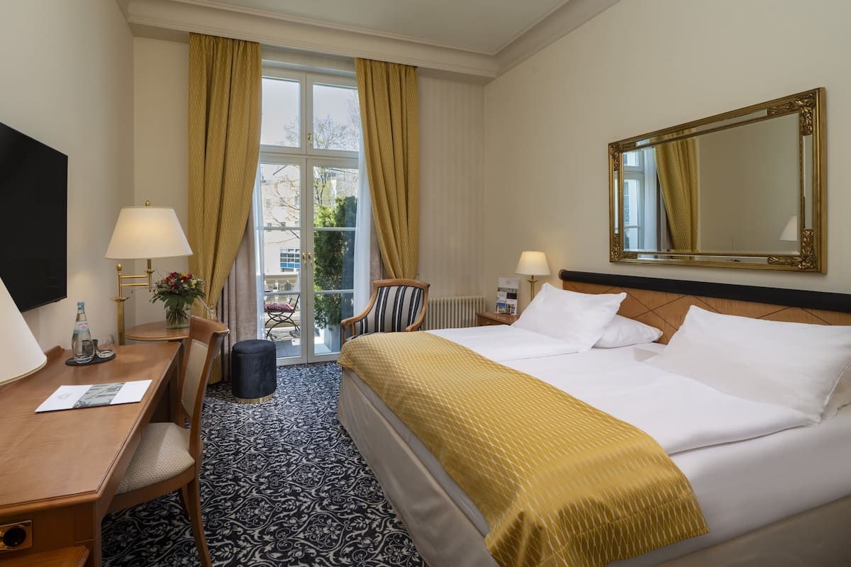 Habitación de hotel con cama, escritorio con lámpara, silla, televisor y un espejo grande.