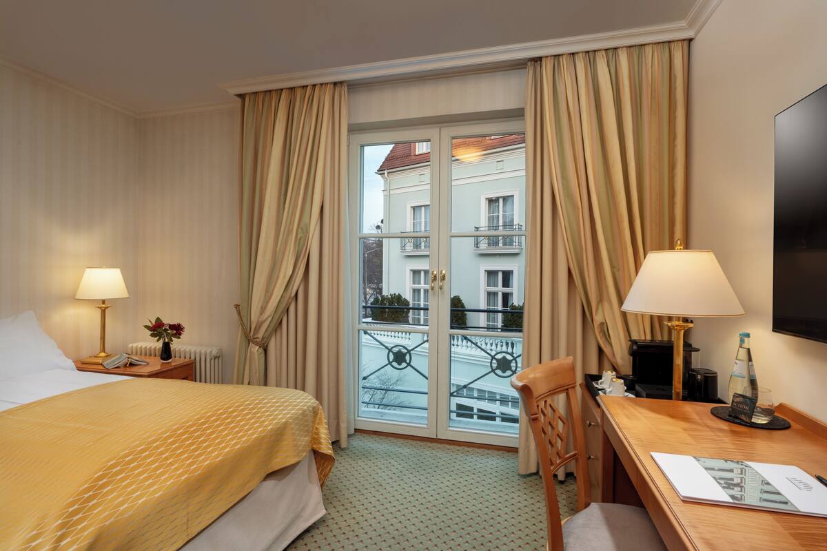 Habitación de hotel con cama, escritorio, silla, televisor y ventana con cortinas.