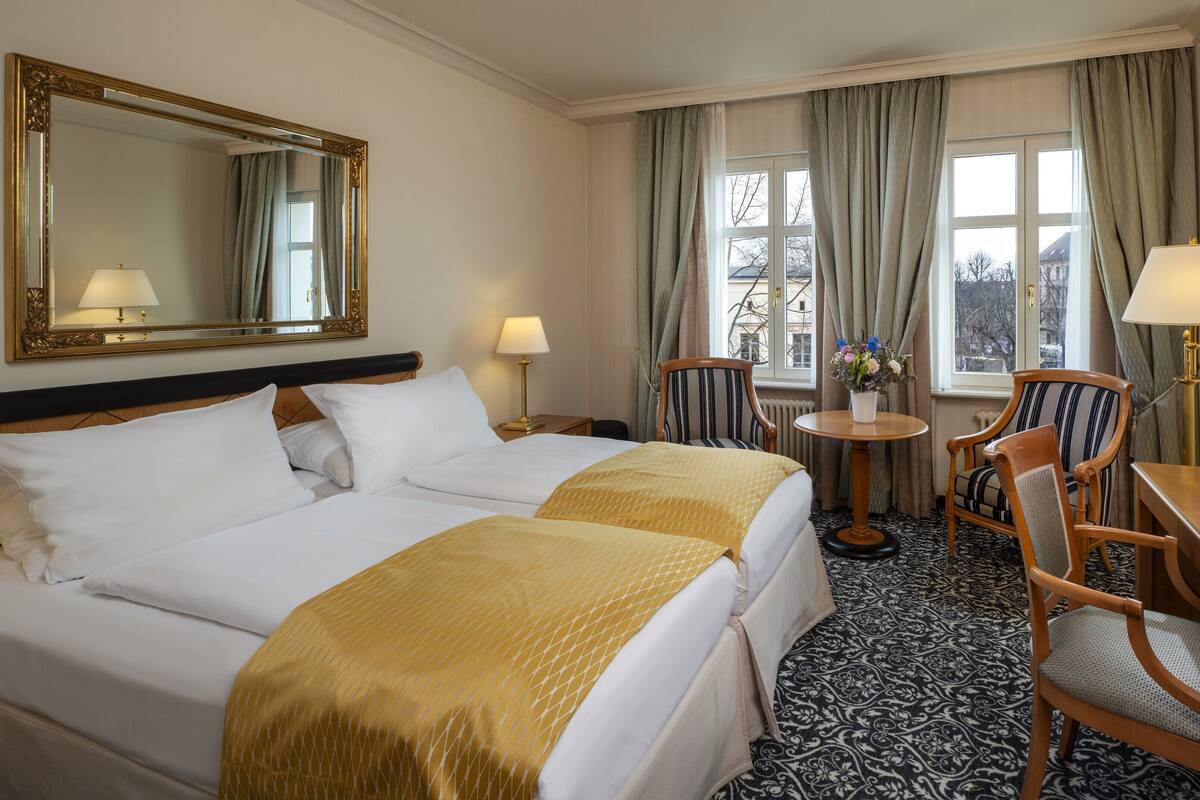 Una habitación de hotel con dos camas, un escritorio, una silla, una mesa redonda y un espejo grande.
