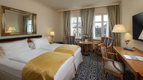 A hotel room with two beds, a desk, a chair, a round table, and a large mirror.