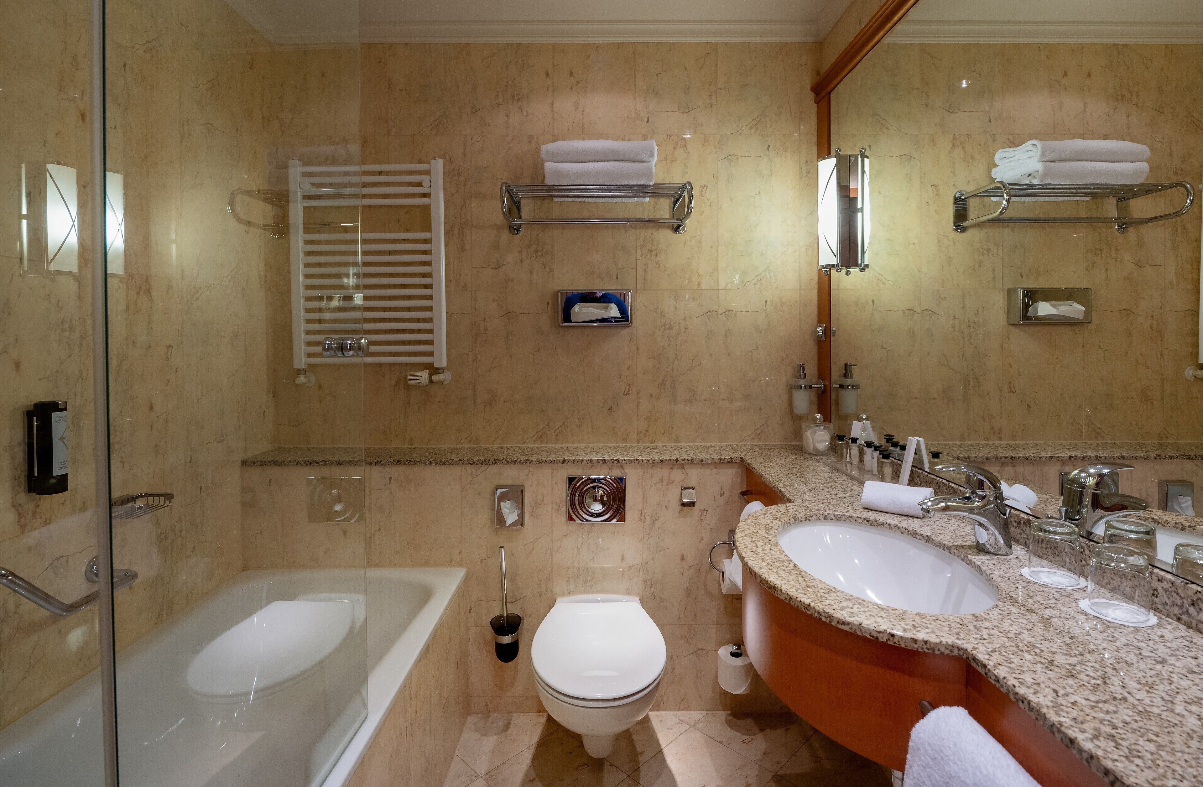 Une salle de bain moderne avec une douche à parois de verre, des toilettes blanches, un lavabo avec un plan de travail en granit et un grand miroir.