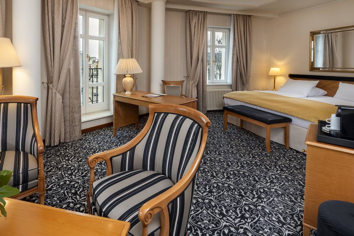 Habitación de hotel con cama, escritorio, dos sillas, una mesa con un arreglo floral y un televisor.