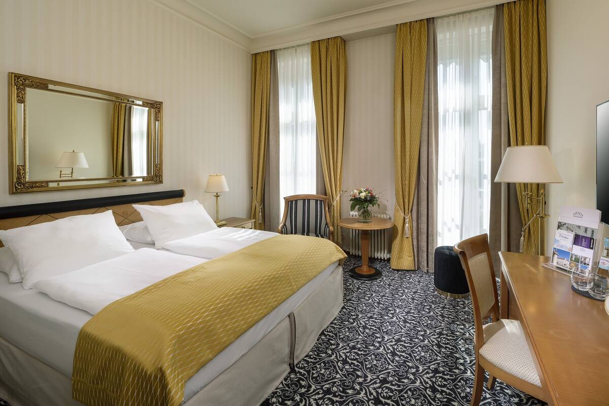 Habitación de hotel con una cama grande, un escritorio con silla, un televisor y un espejo.