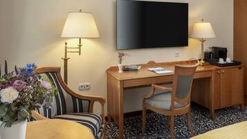 A hotel room with a wooden desk, two chairs, a television, a coffee maker, and a flower vase.