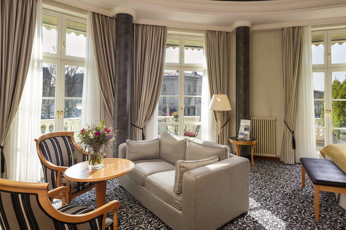 Habitación de hotel con sofá, una silla, una mesita con un jarrón de flores, una lámpara y una cama.