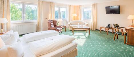 Habitación de hotel con una cama grande, dos sillones, una mesa de centro, un escritorio con una computadora y un televisor en la pared.