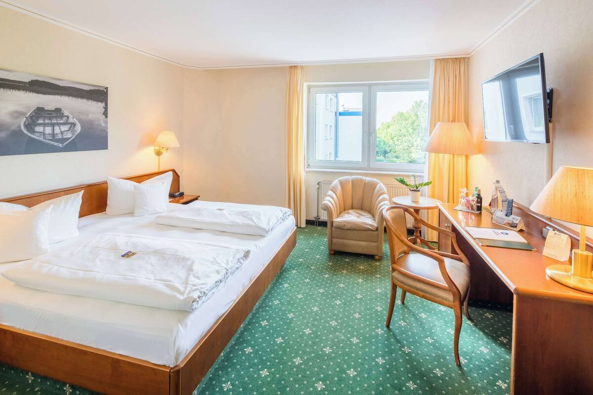 A hotel room with a large bed, a desk with a chair, a TV, and a window with curtains.