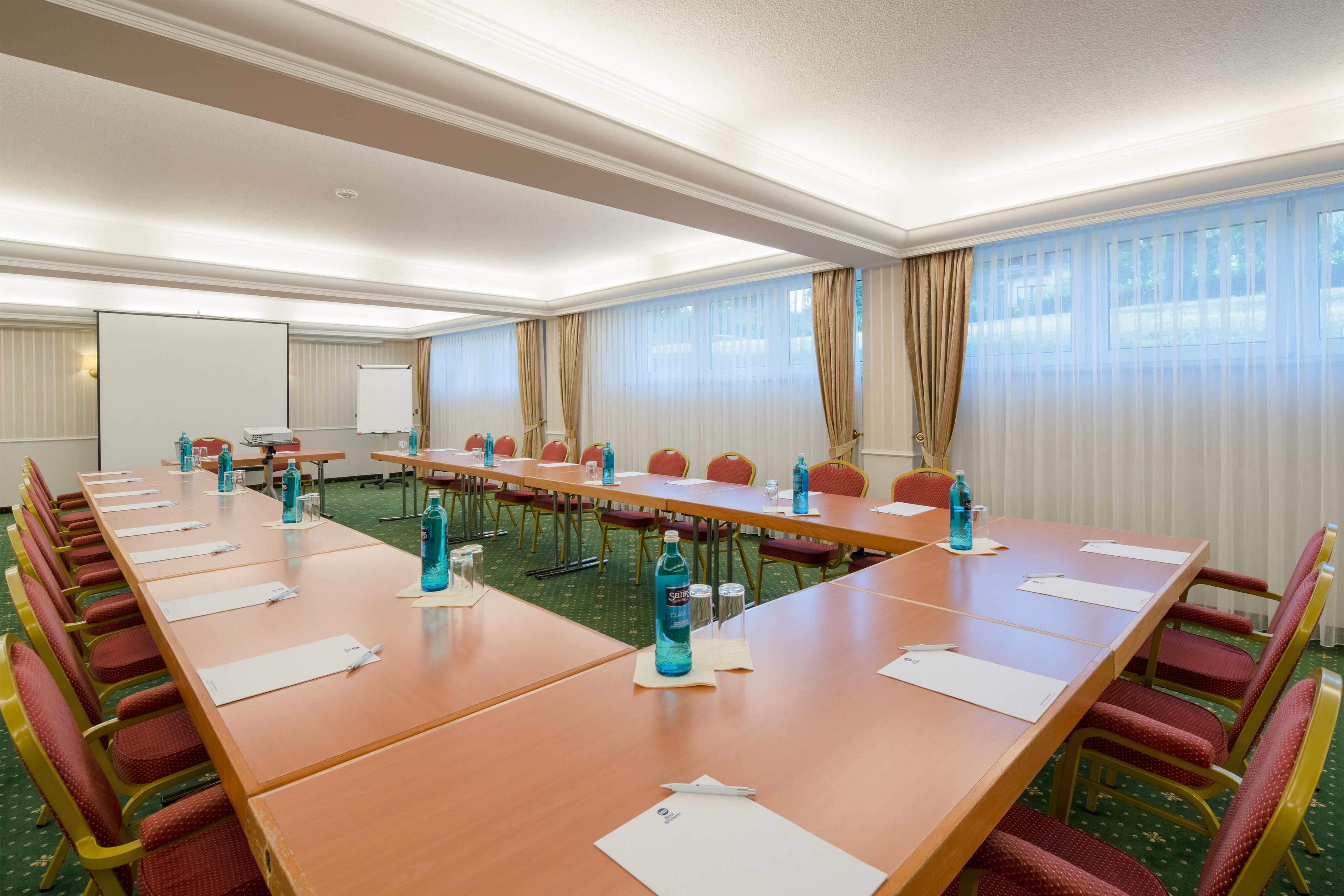A conference room with a long table, chairs, and a projector screen.