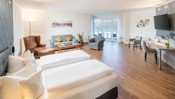 A modern hotel room with a large bed, a sofa, a dining area, and a balcony with a view.