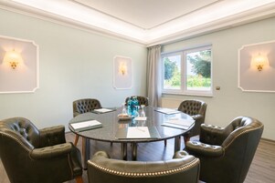 Un salón de conferencias con una mesa redonda, seis sillas de cuero y dos lámparas de pared.