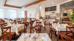 Une salle à manger d’hôtel avec plusieurs tables dressées pour les clients, un bar et un écran de télévision.