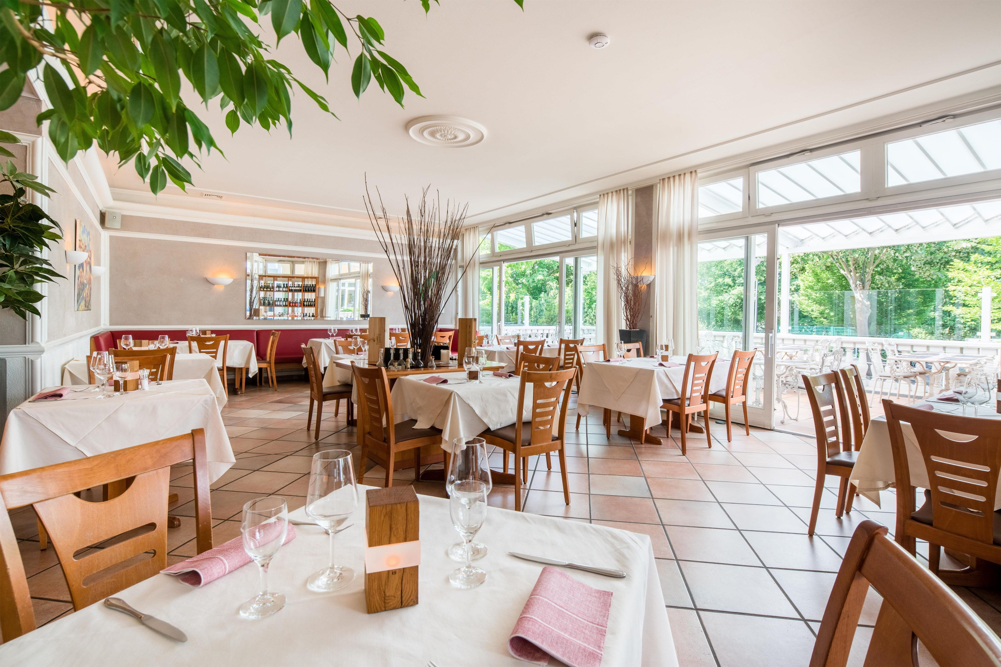 En restaurant med dækketøjsbestik, et barområde og store vinduer med udsigt over det fri.