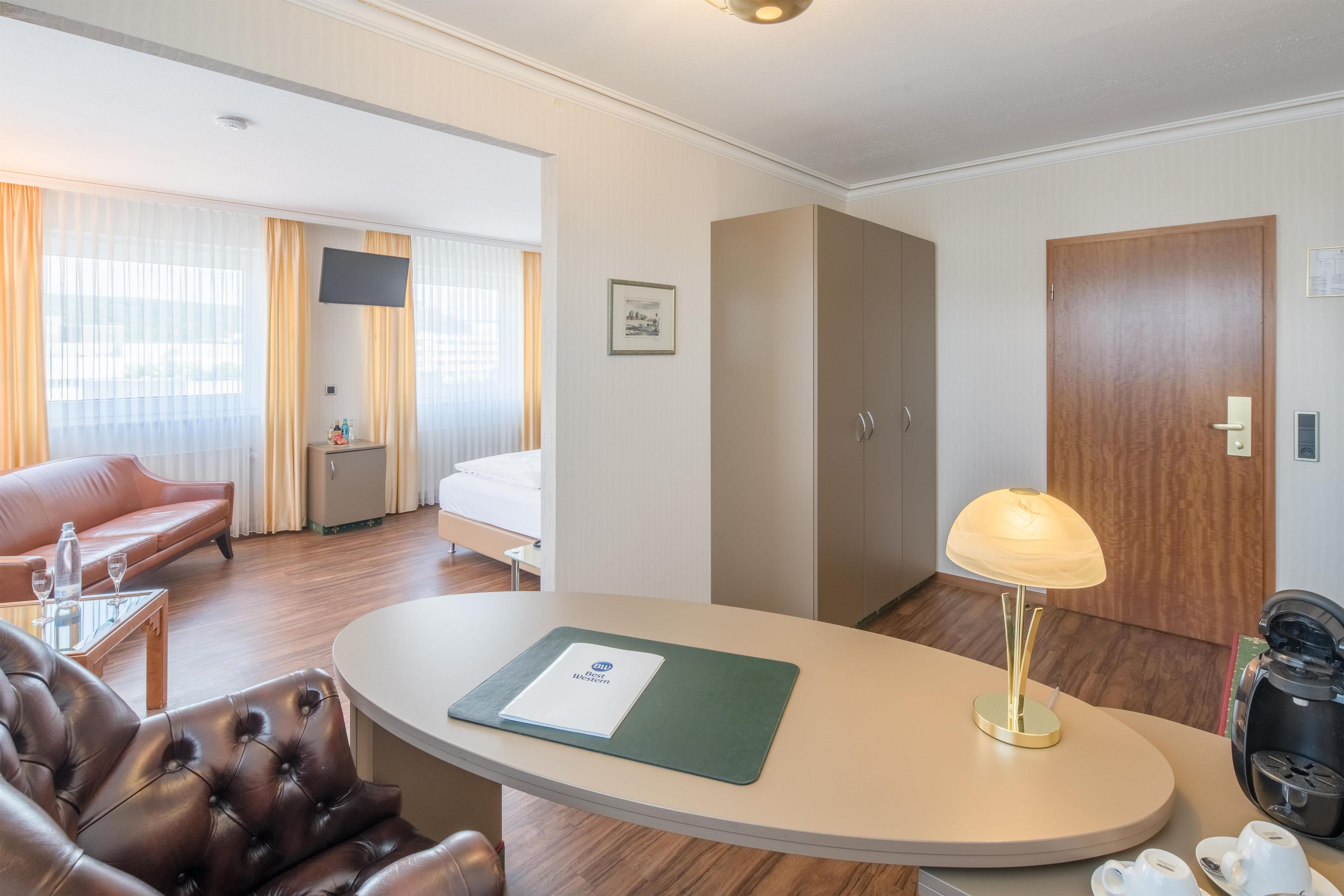 Habitación de hotel con cama, sofá, escritorio con lámpara, cafetera y televisión.