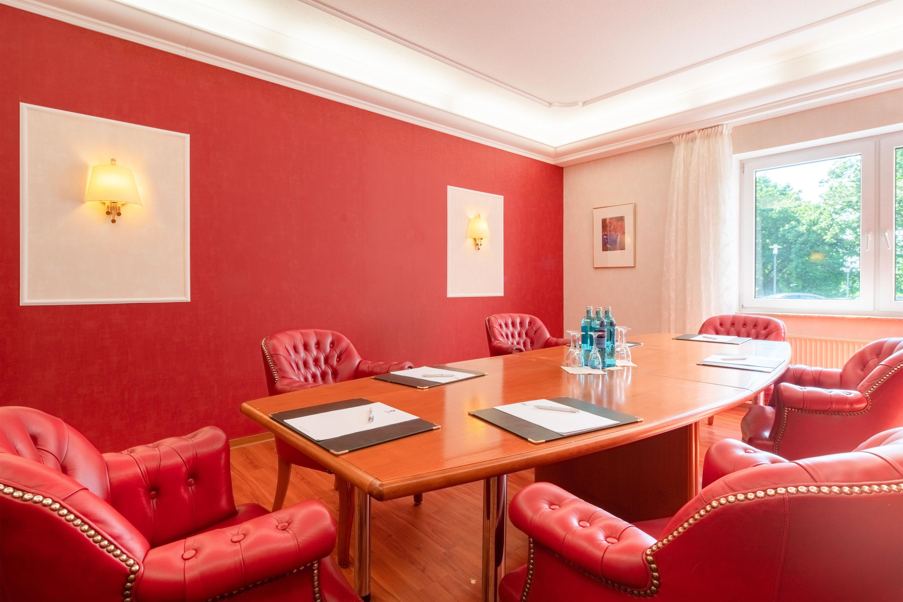 Un salón de conferencias con una mesa de madera, sillas de cuero rojo y dos lámparas fijadas a la pared.