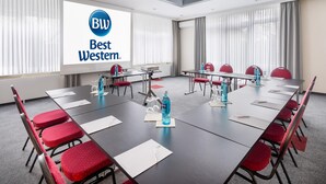 Une salle de conférence dotée d’un grand écran affichant le logo « BW Best Western », de plusieurs tables avec des chaises et de bouteilles d’eau posées sur les tables.