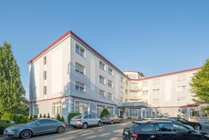 Un hotel de varios pisos con fachada blanca y detalles en rojo, que cuenta con un estacionamiento y varios automóviles.