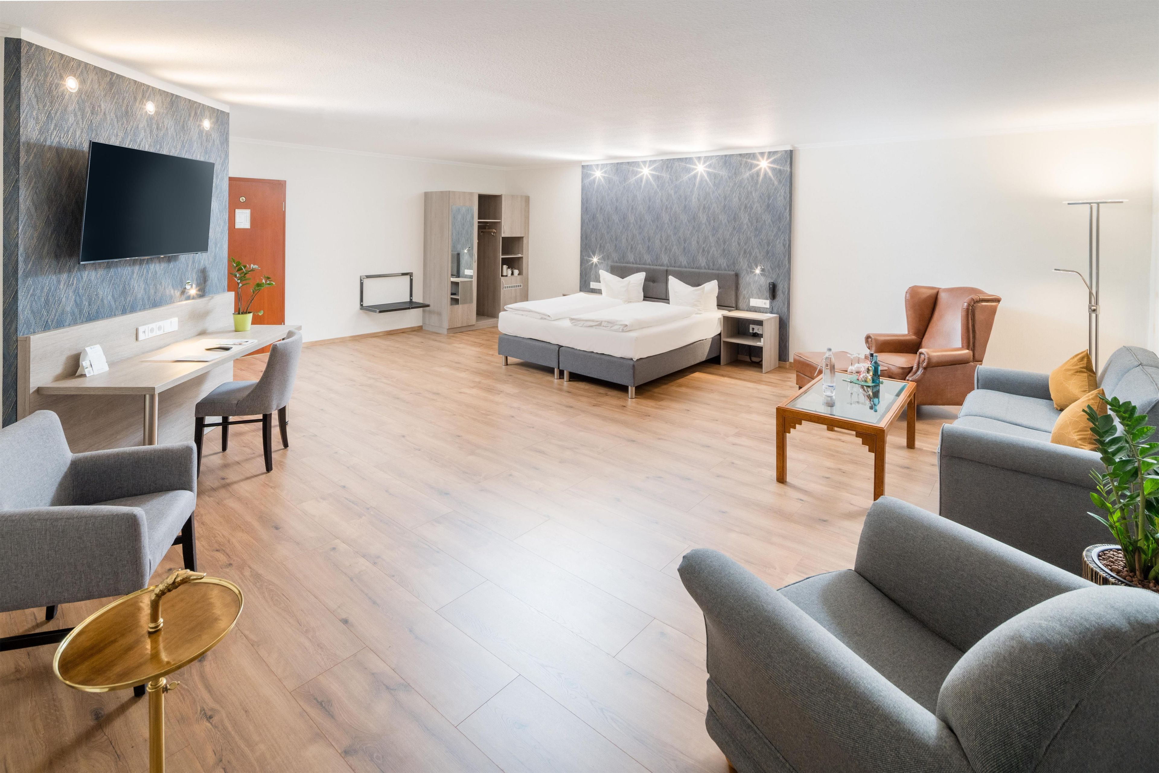 Una habitación de hotel moderna con televisión de pantalla plana, un escritorio, una cama, un área de estar con una mesita de centro y un armario.