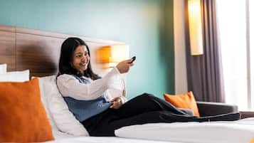 En person sidder på en seng i et hotelværelse med en trægavl, puder og en lampe.
