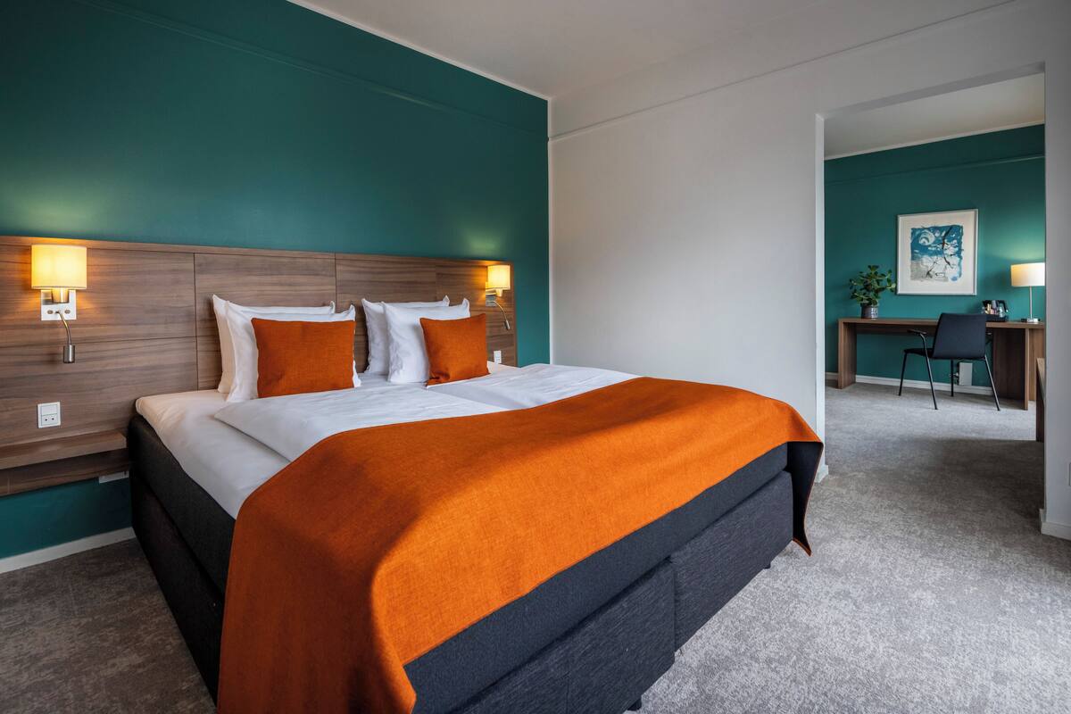 Et hotelværelse med en stor seng, turkis vægge og et skrivebord.