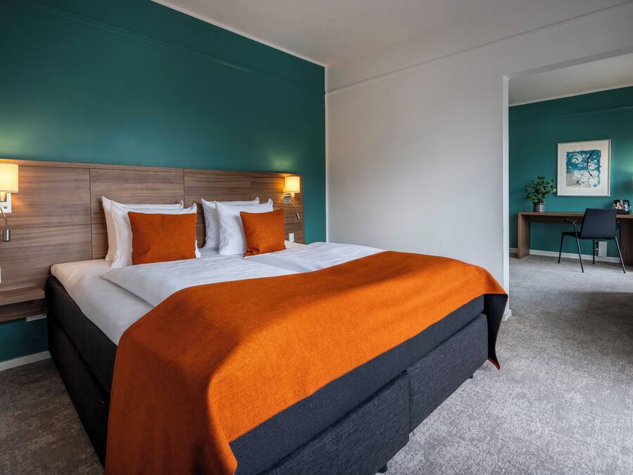 A hotel room with a large bed, teal walls, and a desk area.