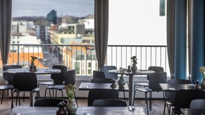 A modern dining area with round tables and chairs, large windows with a city view, and a balcony with a railing. - Hotel Atlantic (Aarhus)
