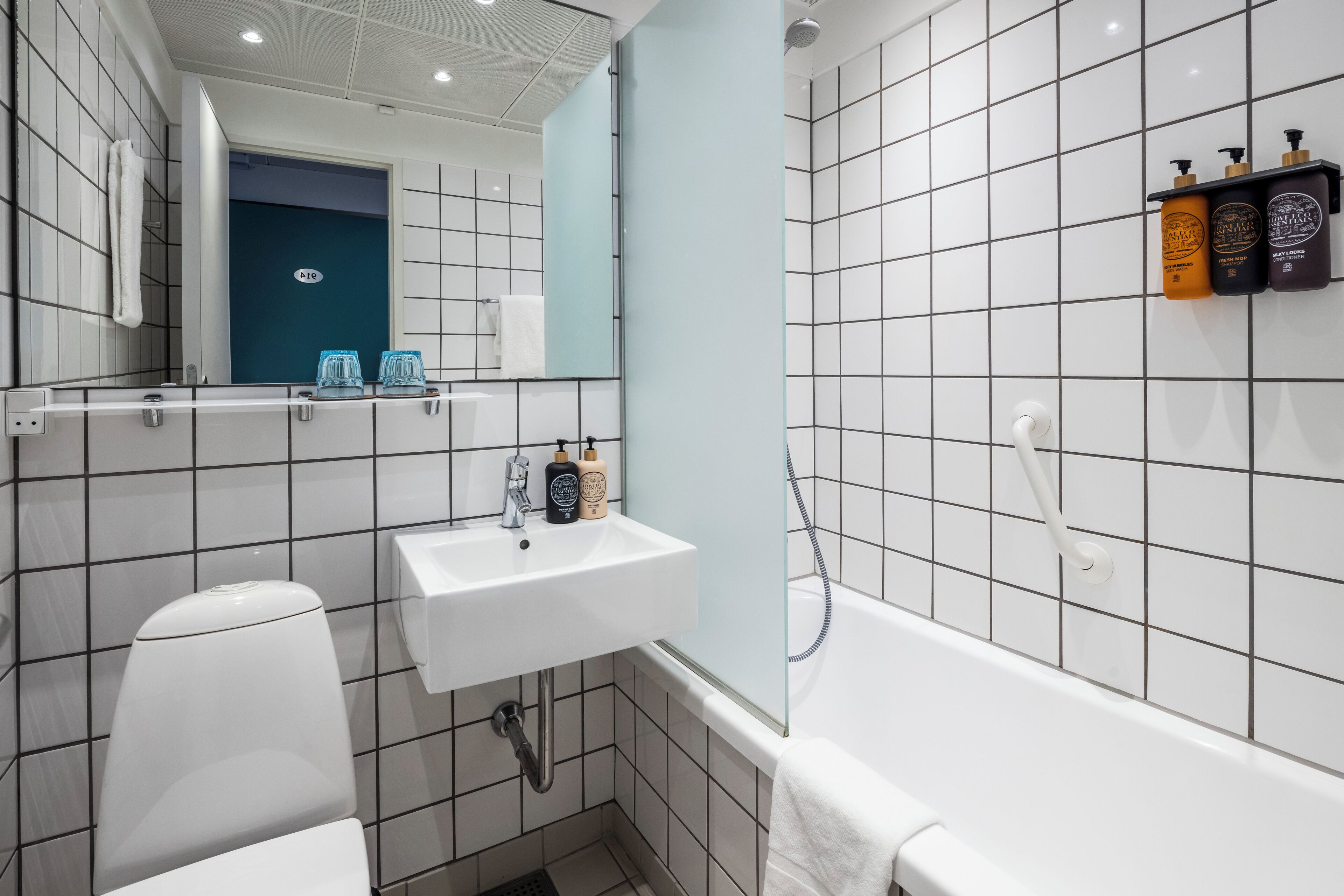 A modern bathroom with a white sink, toilet, and bathtub. There is a mirror above the sink and a towel hanging on the wall.