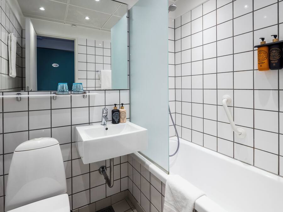 A modern bathroom with a white sink, toilet, and bathtub. There is a mirror above the sink and a towel hanging on the wall.