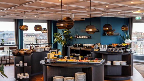 A modern breakfast bar with a variety of food options and a view of the city. - Hotel Atlantic (Aarhus)