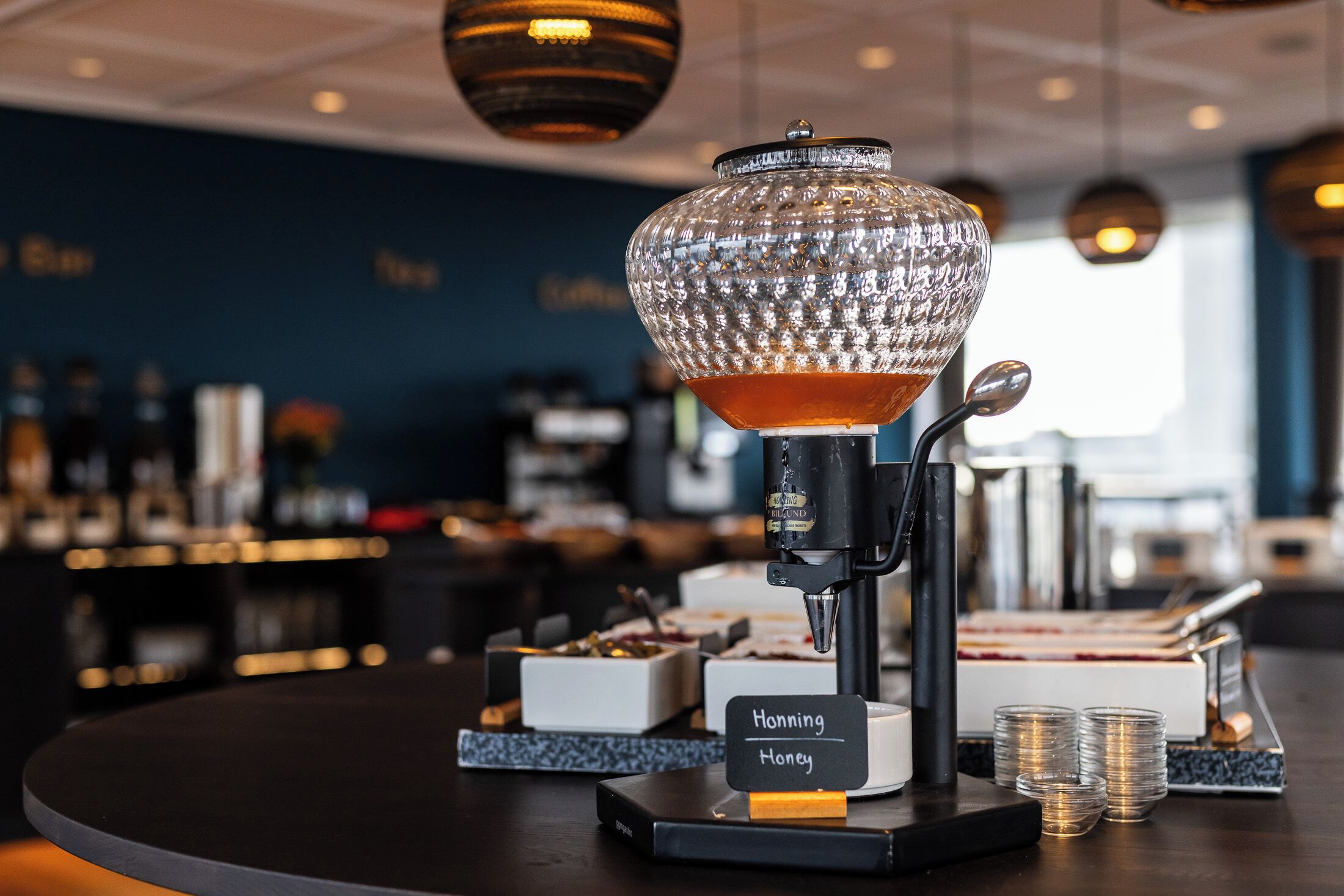 Una zona de bar con una máquina de café, un recipiente de vidrio con la etiqueta 'Honey' y montones de monedas.