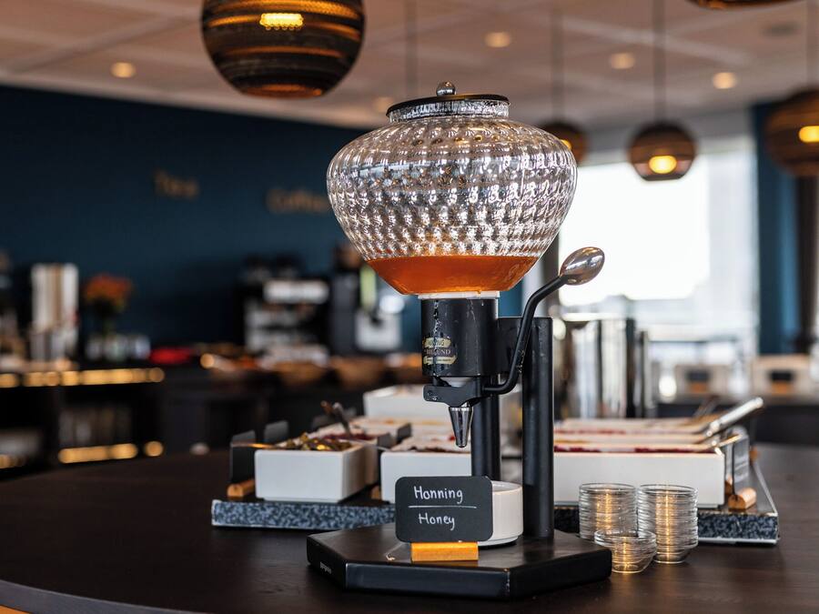 Una zona de bar con una máquina de café, un recipiente de vidrio con la etiqueta 'Honey' y montones de monedas.