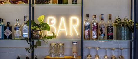 A bar area with shelves of liquor bottles, a neon 'BAR' sign, and a selection of glasses.