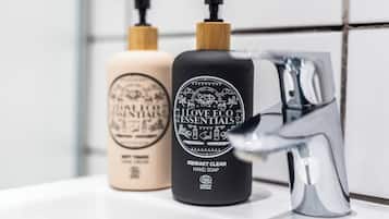 Dos botellas de jabón para manos sobre una superficie blanca junto a un grifo moderno.