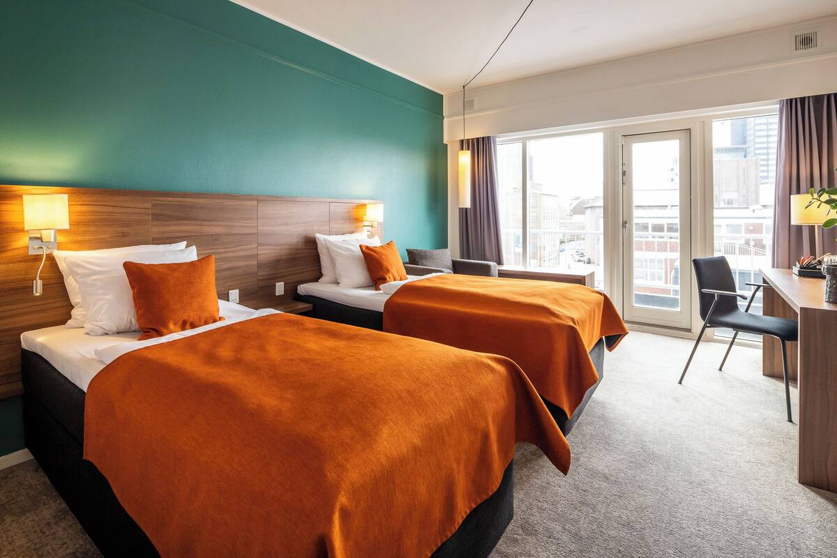 Et hotelværelse med to senge, et skrivebord og en stol.