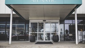 The entrance to the Atlantic Hotel with a modern design, featuring a teal awning, large glass doors, and two potted plants at the entrance. - Hotel Atlantic (Aarhus)