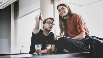 Dos personas sentadas en una mesa con bebidas, en una habitación con amplios ventanales y diseño moderno.