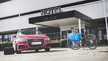Ein roter Audi parkt vor einem Hotel namens "ATLANTIC". Ein Fahrrad und eine blaue Tasche befinden sich in der Nähe.