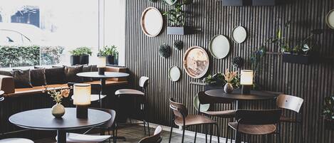 A modern cafe interior with round tables, chairs, and a variety of plants on shelves.