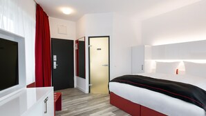 Una habitación de hotel con una cama, televisión, escritorio y armario.