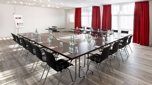 Un salón de conferencias con una mesa larga, sillas negras y cortinas rojas.