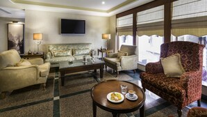 A spacious living room with a sofa, armchairs, a coffee table, and a flat-screen TV mounted on the wall.