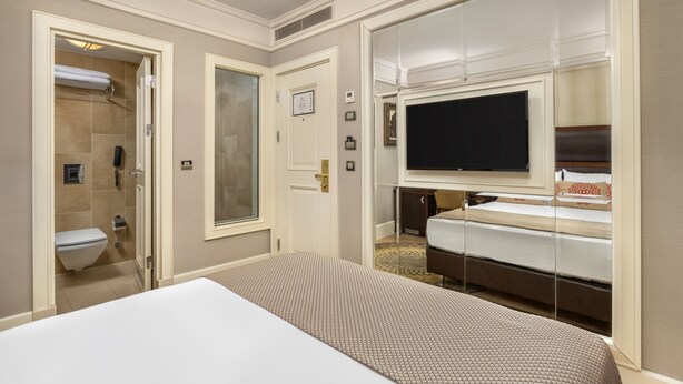 A hotel room with a bed, a television, a bathroom with a toilet and shower, and a minibar.