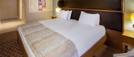 Una cama grande con cabecera, dos mesitas de noche con lámparas, una silla y suelo cubierto de alfombra.